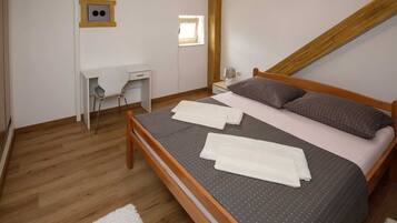A bedroom with a wooden bed, a desk, a chair, and a small window.