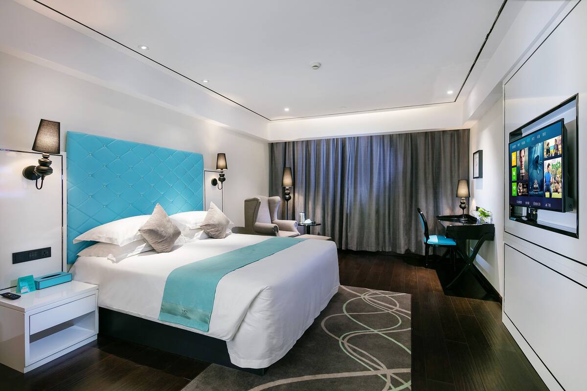 A modern hotel room with a large bed, a desk, a chair, and a flat-screen TV.