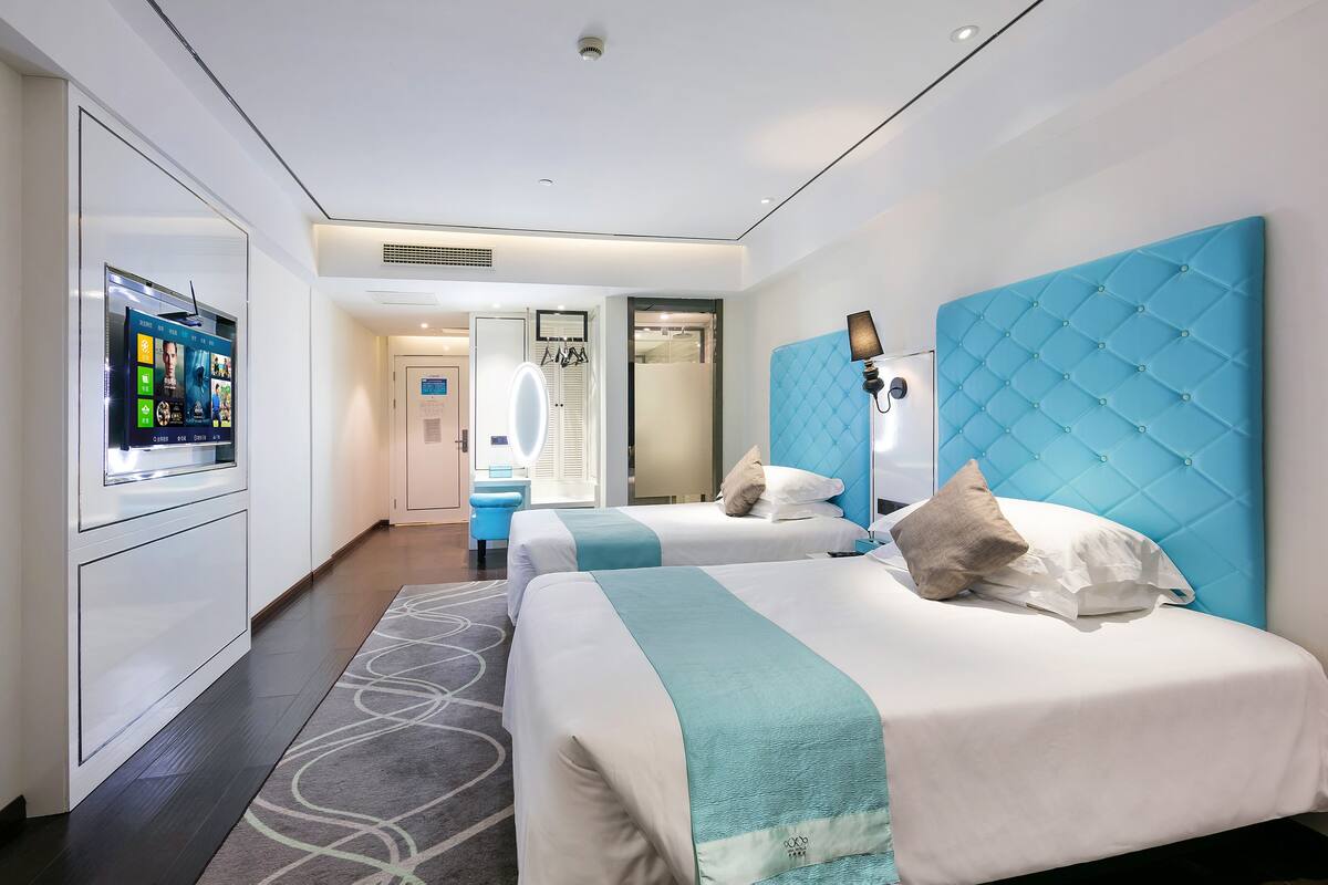 A hotel room with two beds, a TV, a mirror, and a bathroom visible through an open door.