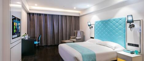 Una habitación de hotel moderna con una cama grande, un escritorio con computadora, una silla y un televisor montado en la pared.