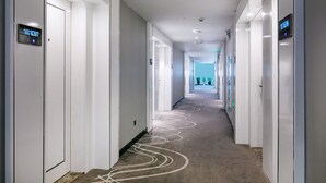 A modern hotel corridor with a carpeted floor, white walls, and doors with digital displays. - Xi'an Hotel Xiaoshan Airport Branch (Hangzhou)