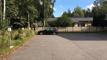 Un parking avec une voiture, entouré d’arbres et d’un bâtiment doté d’un toit en pente.