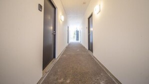 Un couloir étroit, avec des portes de part et d’autre, des luminaires fixés aux murs et un sol recouvert de moquette.