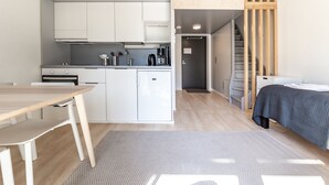 Un angolo cottura compatto con mobili bianchi, un tavolo di legno e un letto con copripiumino blu scuro.