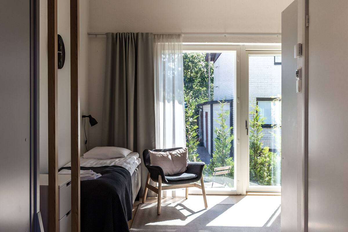 A bedroom with a bed, a chair, a desk, and a sliding door leading to a balcony.