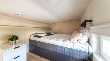 Un dormitorio compacto con una cama, una mesita de noche, una planta pequeña y una ventana.
