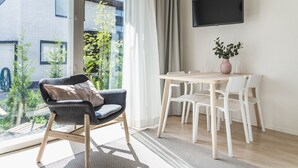 Una camera moderna con un tavolo da pranzo, sedie, una TV e vista su un edificio e sul verde circostante.