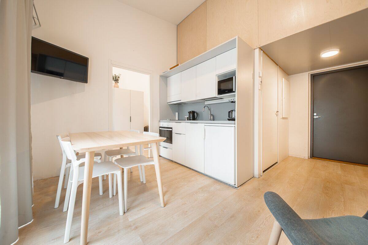 A modern kitchen with white cabinetry, a microwave, and a sink. There is a dining table with chairs and a small plant on the wall.