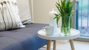 A modern living room with a grey sofa, a white coffee table with a candle and a vase of white flowers, and a patterned rug. - Spot Apartments Airport (Vantaa)