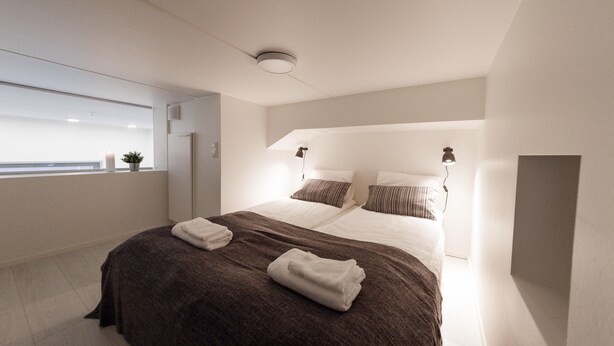 A modern hotel room with a large bed, two bedside lamps, and a view of the city through the window. - Spot Apartments Airport (Vantaa)