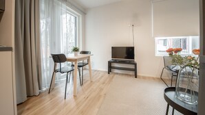Un soggiorno moderno con pavimento in legno, un tavolo da pranzo con due sedie, un televisore a schermo piatto su un mobile e un'ampia finestra con tende.