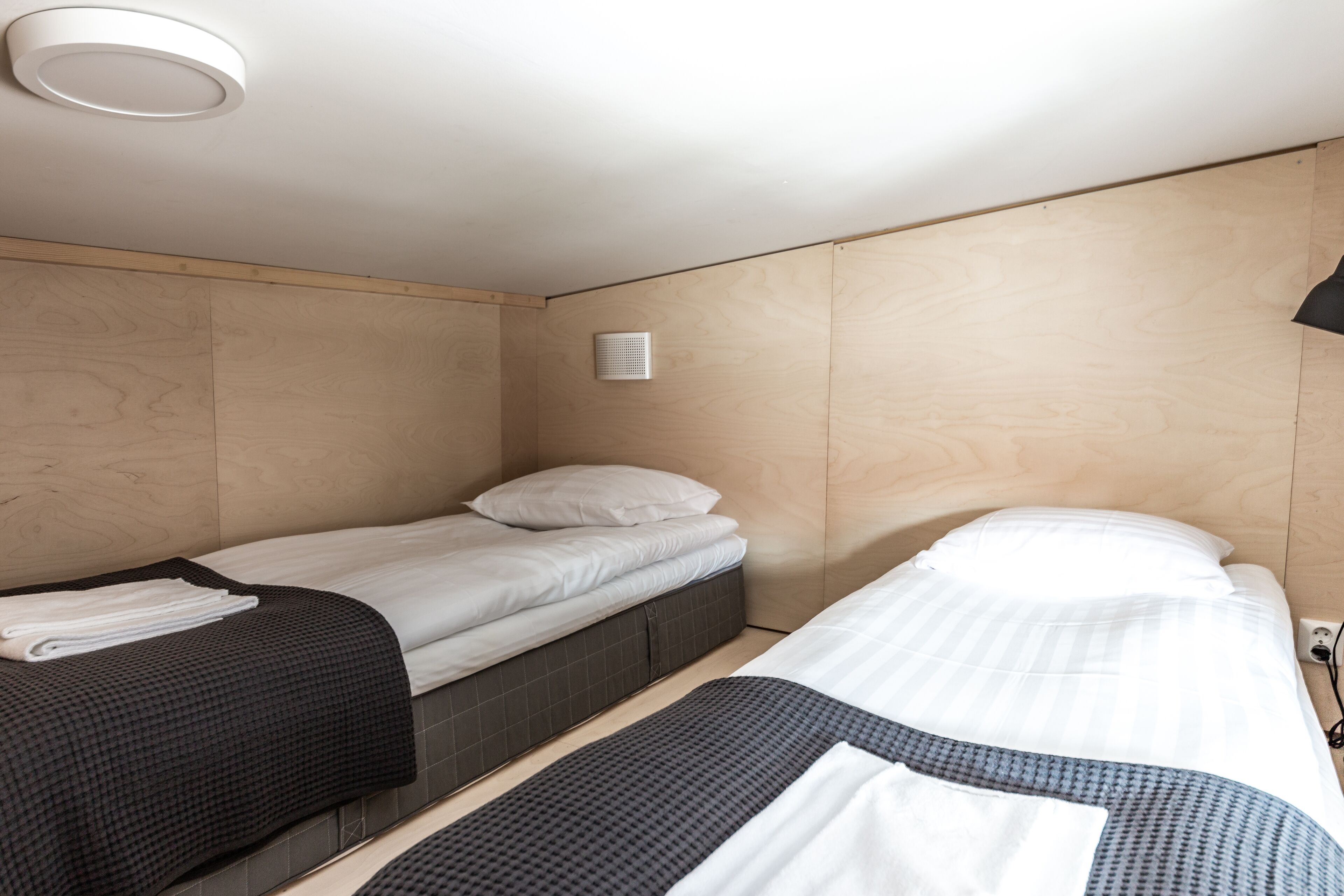 Una habitación de hotel con dos camas, una lámpara de techo y un respiradero en la pared.