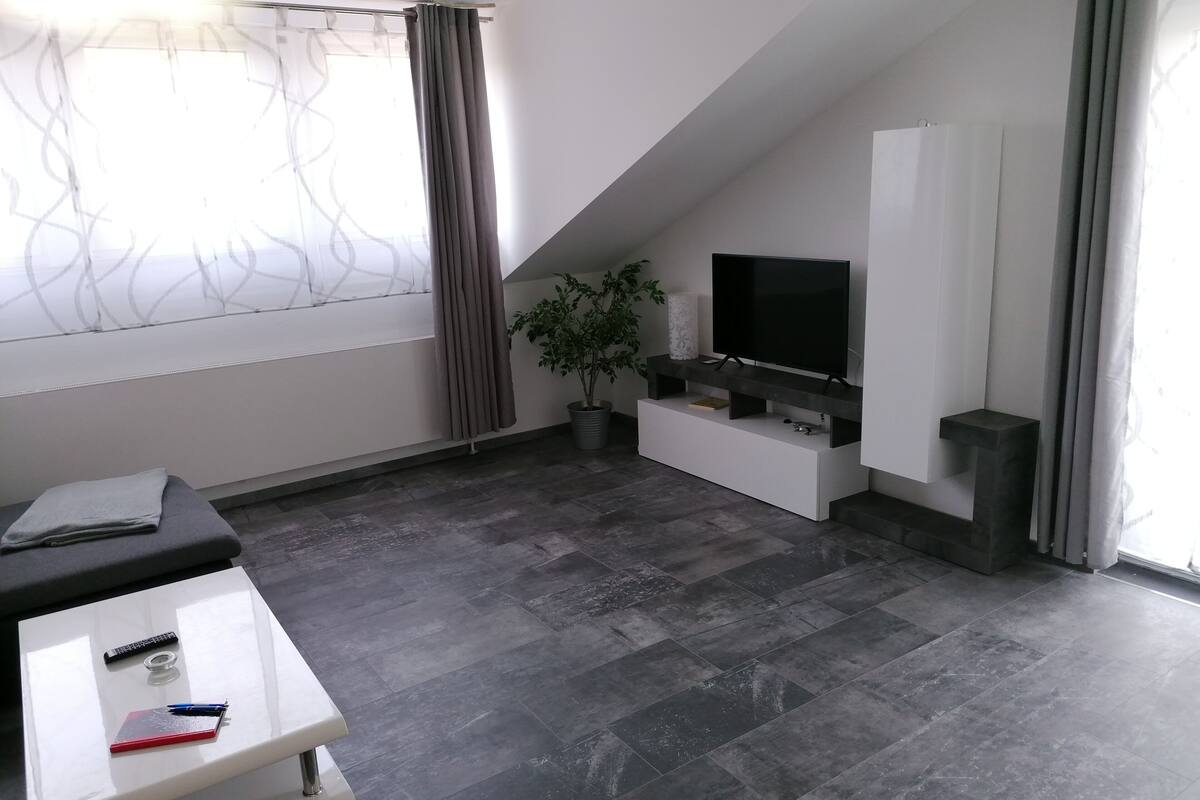 A modern living room with a flat-screen TV, a potted plant, and a white entertainment unit.