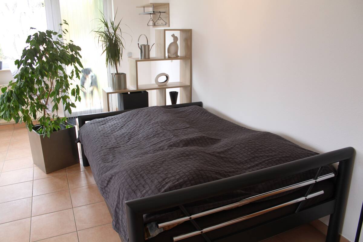 A modern bedroom with a bed, a potted plant, and a small desk with a chair.