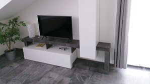 A modern living room with a flat-screen TV on a dark wooden stand, a white cabinet, and a potted plant. - Stollis FeWo (Bensheim)