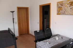 Una habitación pequeña con una cama, una mesa con sillas, una lámpara de pie y una puerta.