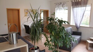 A living room with a grey sofa, a coffee table, and two potted plants. There is a wooden door and a window with curtains. - Stollis FeWo (Bensheim)