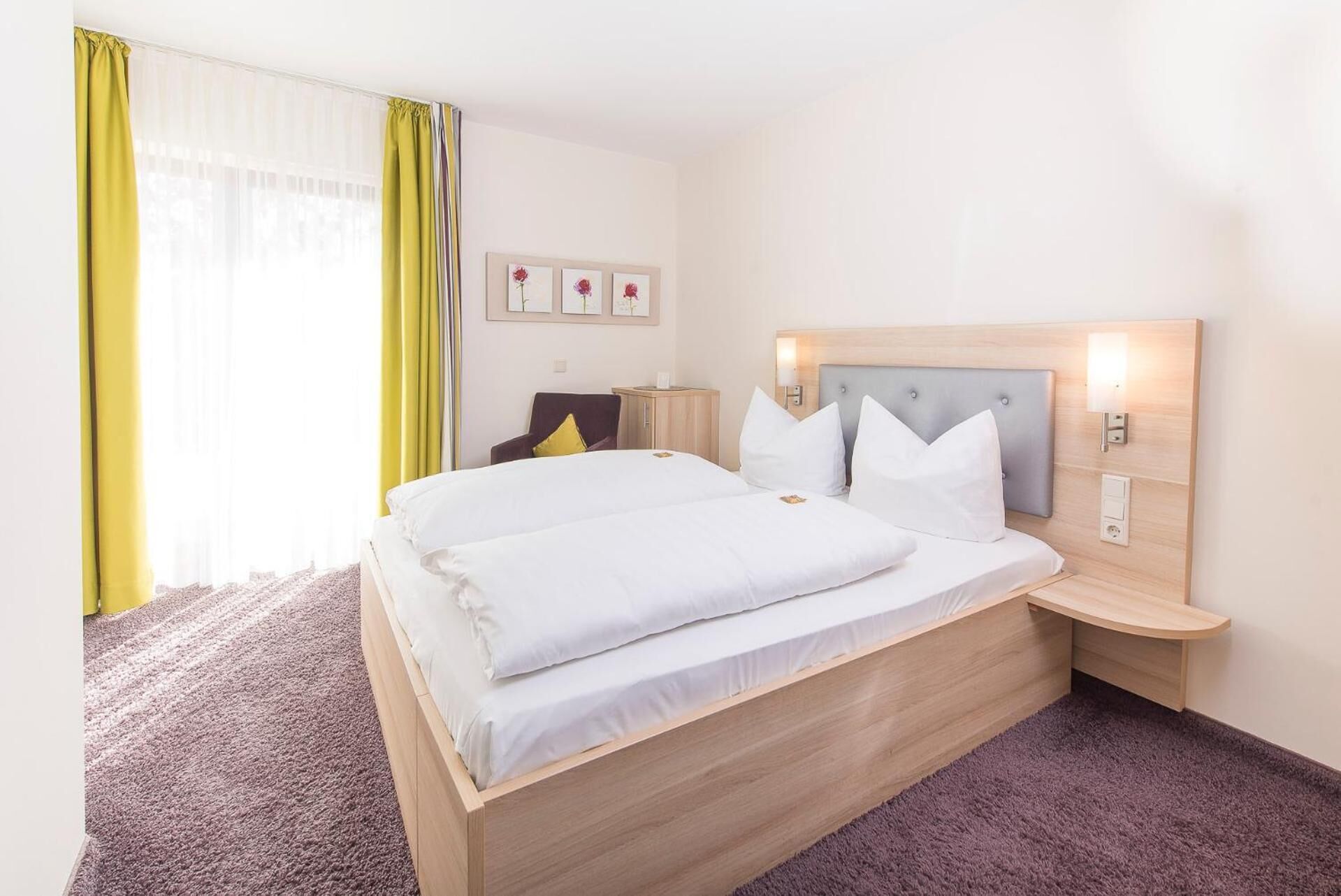 A hotel room with a large bed, a bedside table, a chair, and a desk.