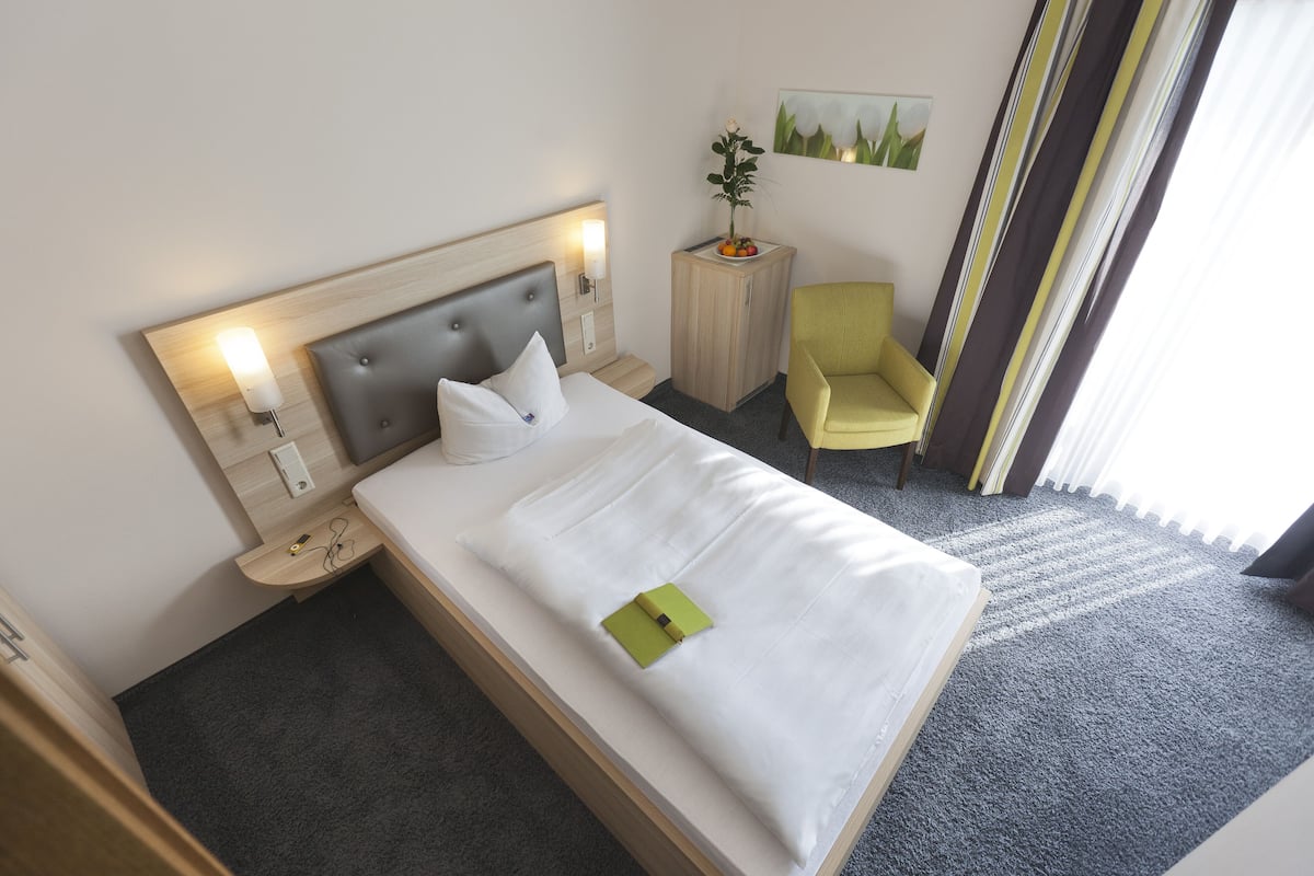 Ein Hotelzimmer mit Bett, Nachttisch, Lampe, Stuhl und einem kleinen Schrank.