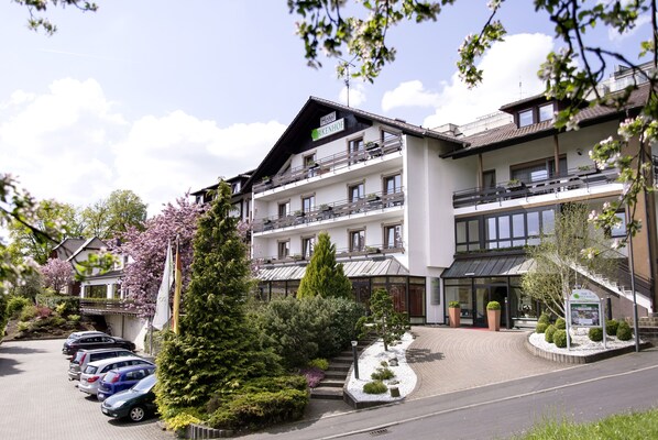 A multi-story hotel with balconies, a parking area, and a well-maintained garden. - Hotel Birkenhof (Bad Soden-Salmuenster)
