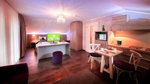 Ein modernes Hotelzimmer mit Holzboden, einer zentralen Insel mit Fernseher, einem Essbereich mit Stühlen und einer Küchenzeile mit Mikrowelle.