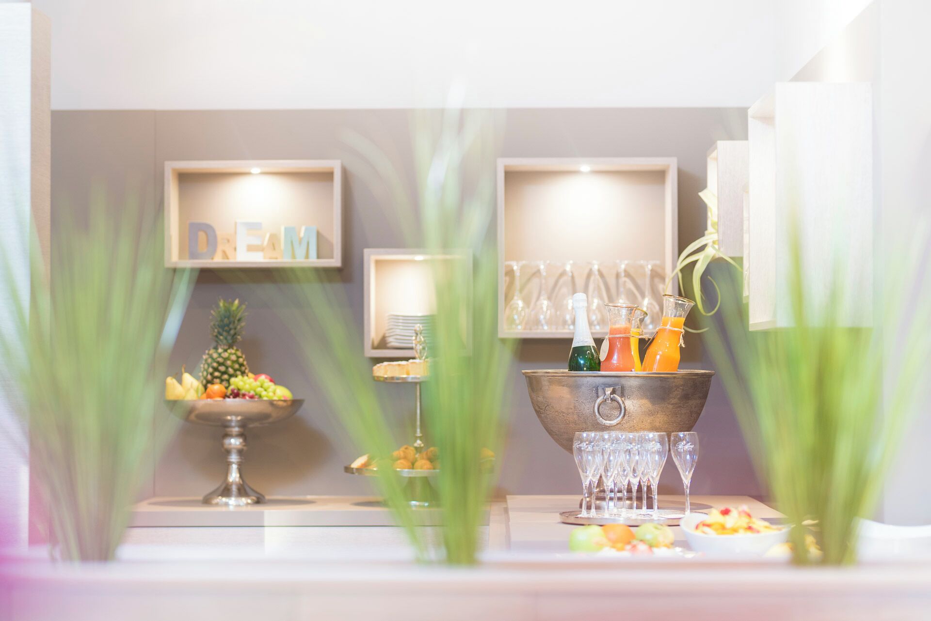 Une pièce bien éclairée, avec un panier de fruits, une bouteille de champagne et un verre de jus d’orange posés sur une table.