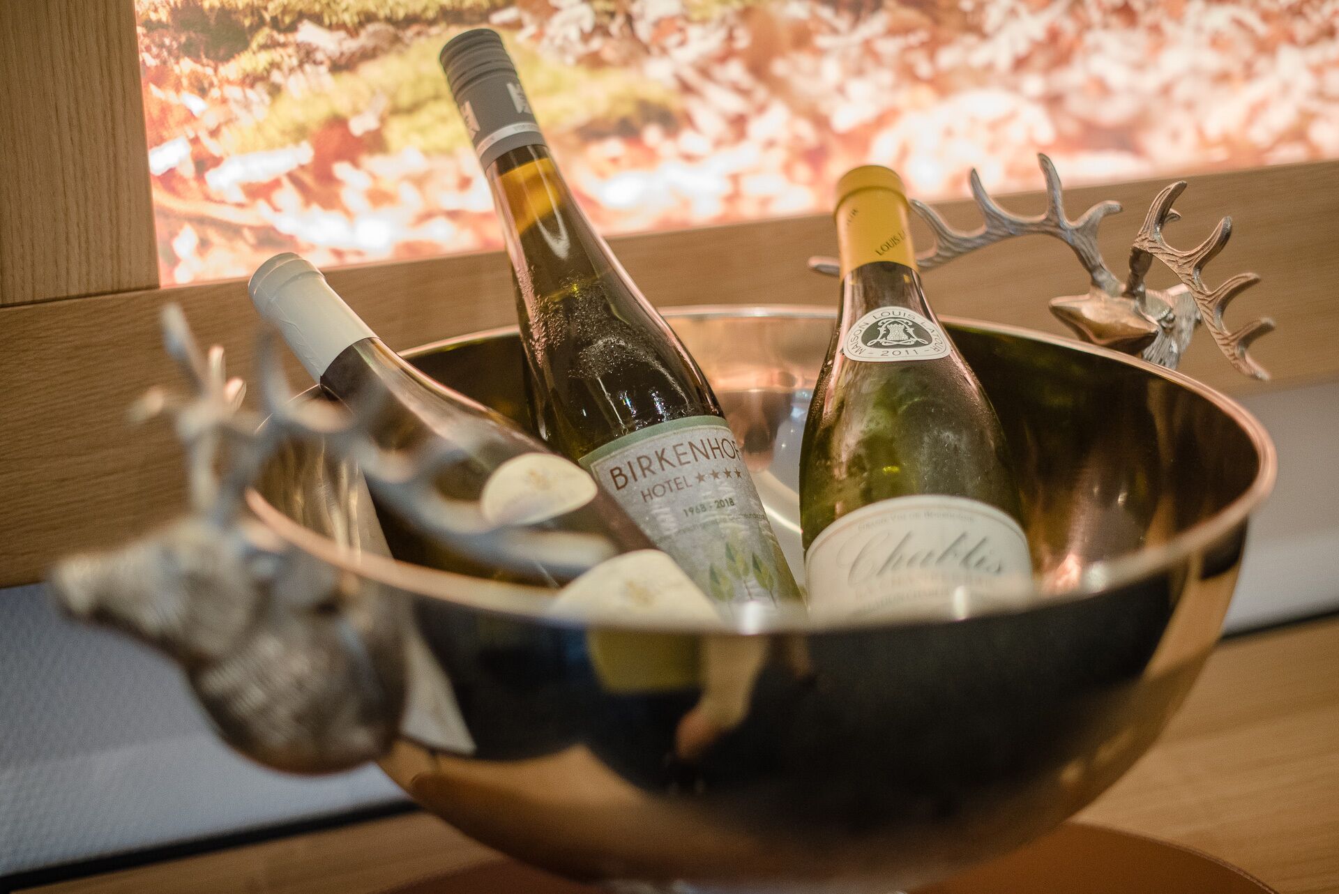 Un tazón metálico que contiene dos botellas de vino, una con la etiqueta 'Birkenhof Hotel' y la otra 'Chablis'.