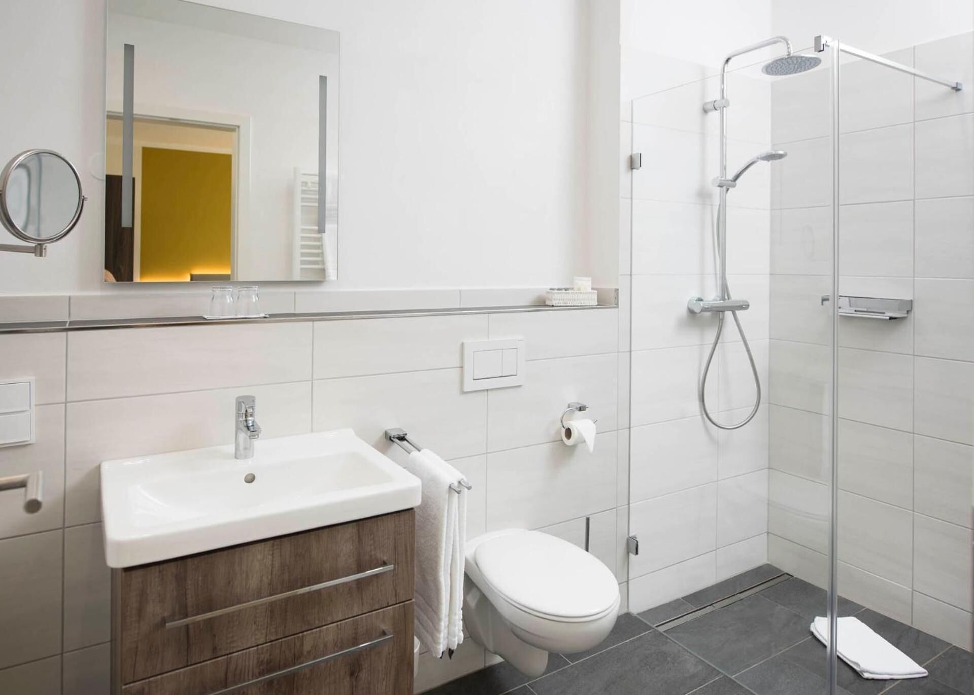 A modern bathroom with a white sink, mirror, toilet, and shower.