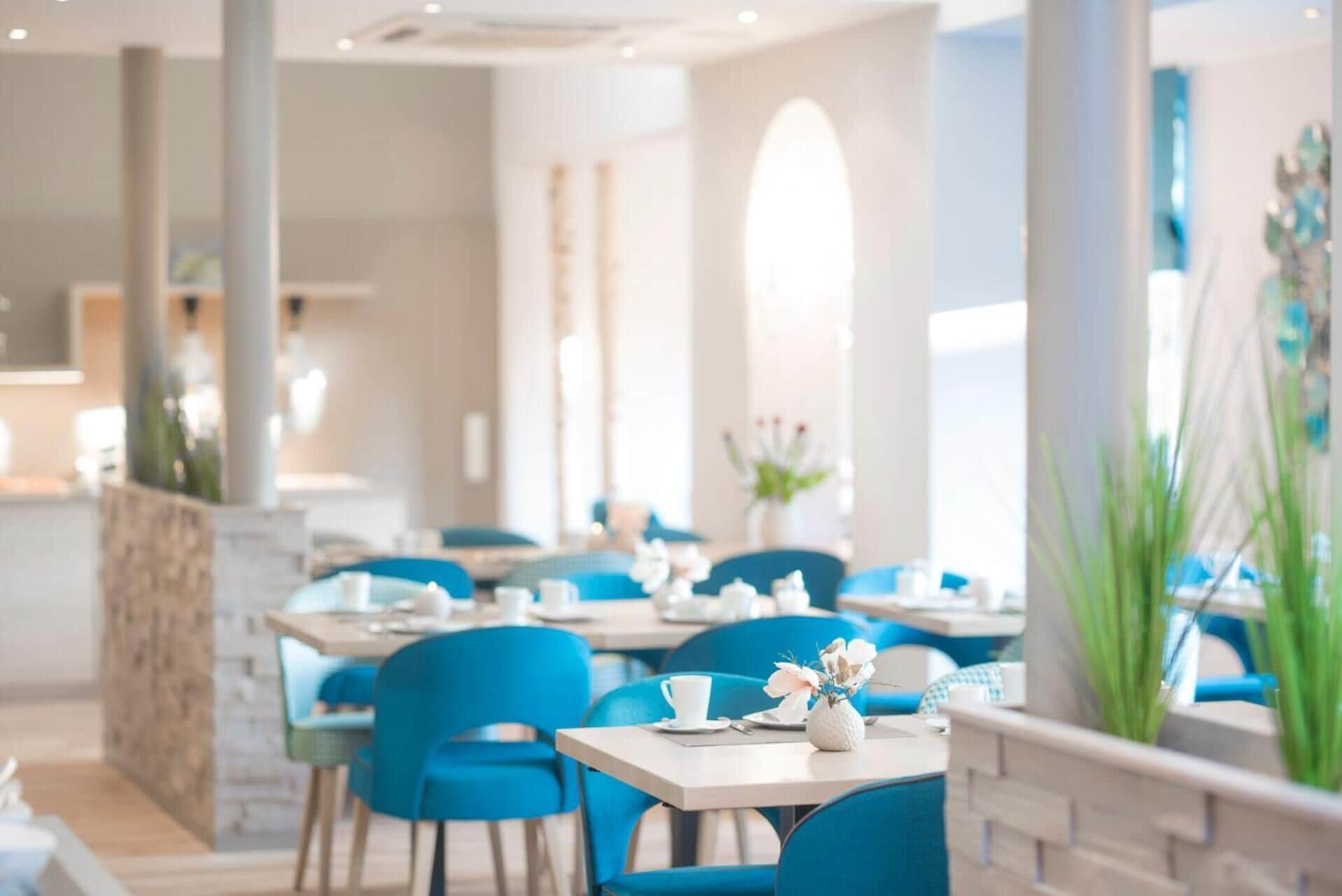 Een modern restaurant met blauwe stoelen en witte tafels, met een stenen pilaar en een groot raam.