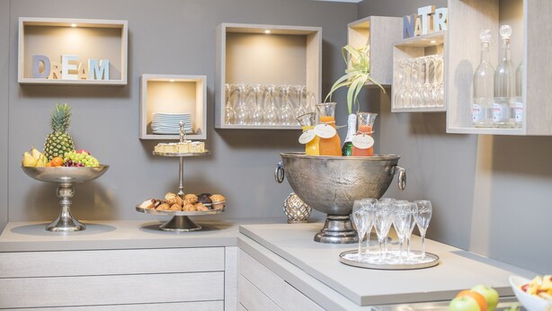 Ein Buffet mit Obst, Gebäck und einer Getränkestation, ergänzt durch gerahmte Sprüche an der Wand.