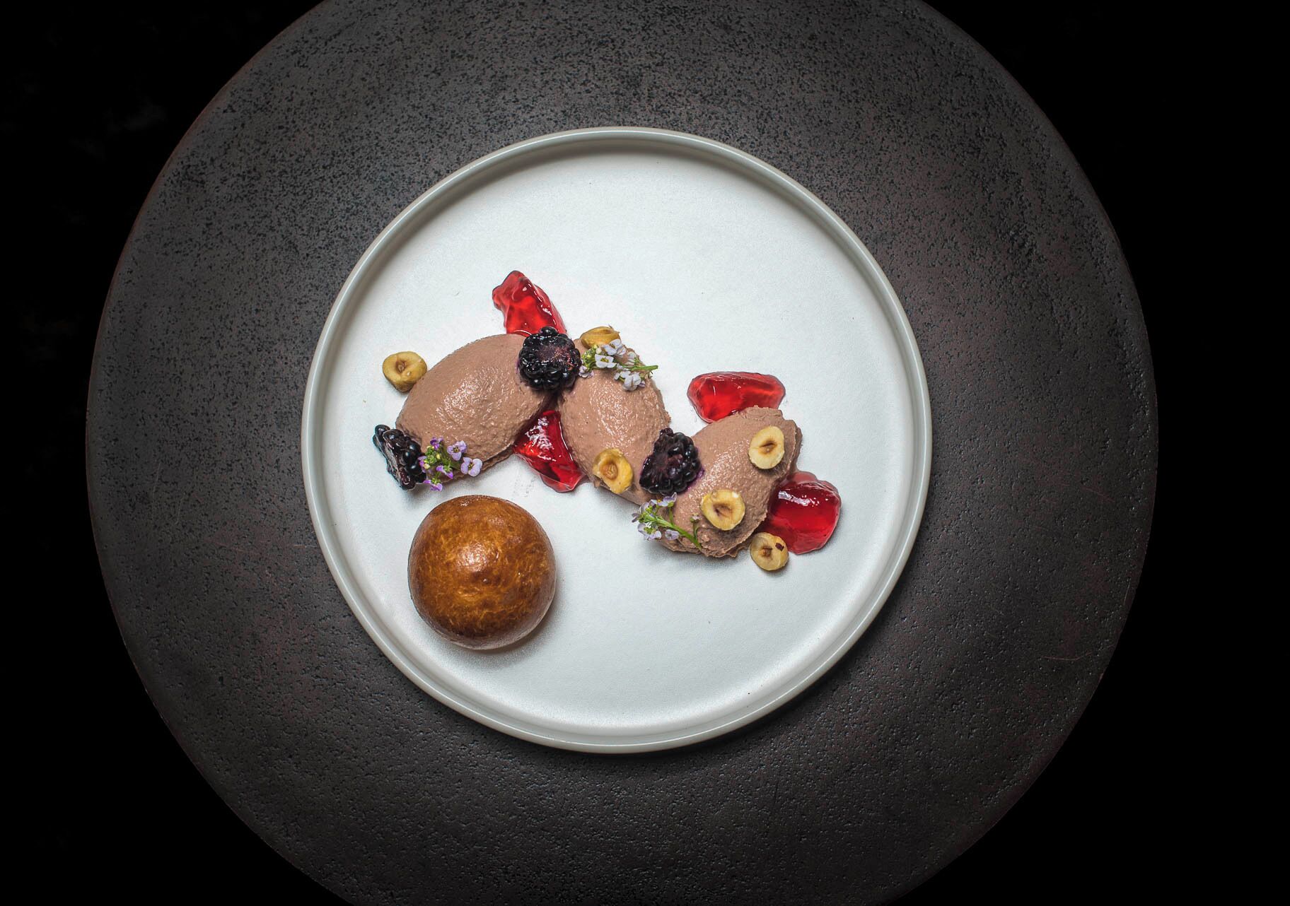 A plate with food items including a round pastry and slices of meat with berries and nuts.