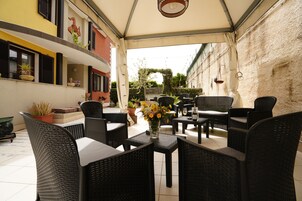An outdoor patio with wicker furniture, a vase of flowers, and a view of the street.