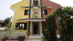 Una casa de dos pisos con balcón, un pequeño jardín con macetas y una puerta con panel de vidrio.