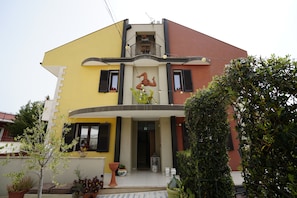 A two-story house with a balcony, a small garden area with potted plants, and a door with a glass panel. - Terra Mia Affittacamere (Melilli)