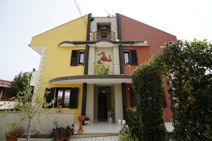 A two-story house with a balcony, a small garden area with potted plants, and a door with a glass panel.