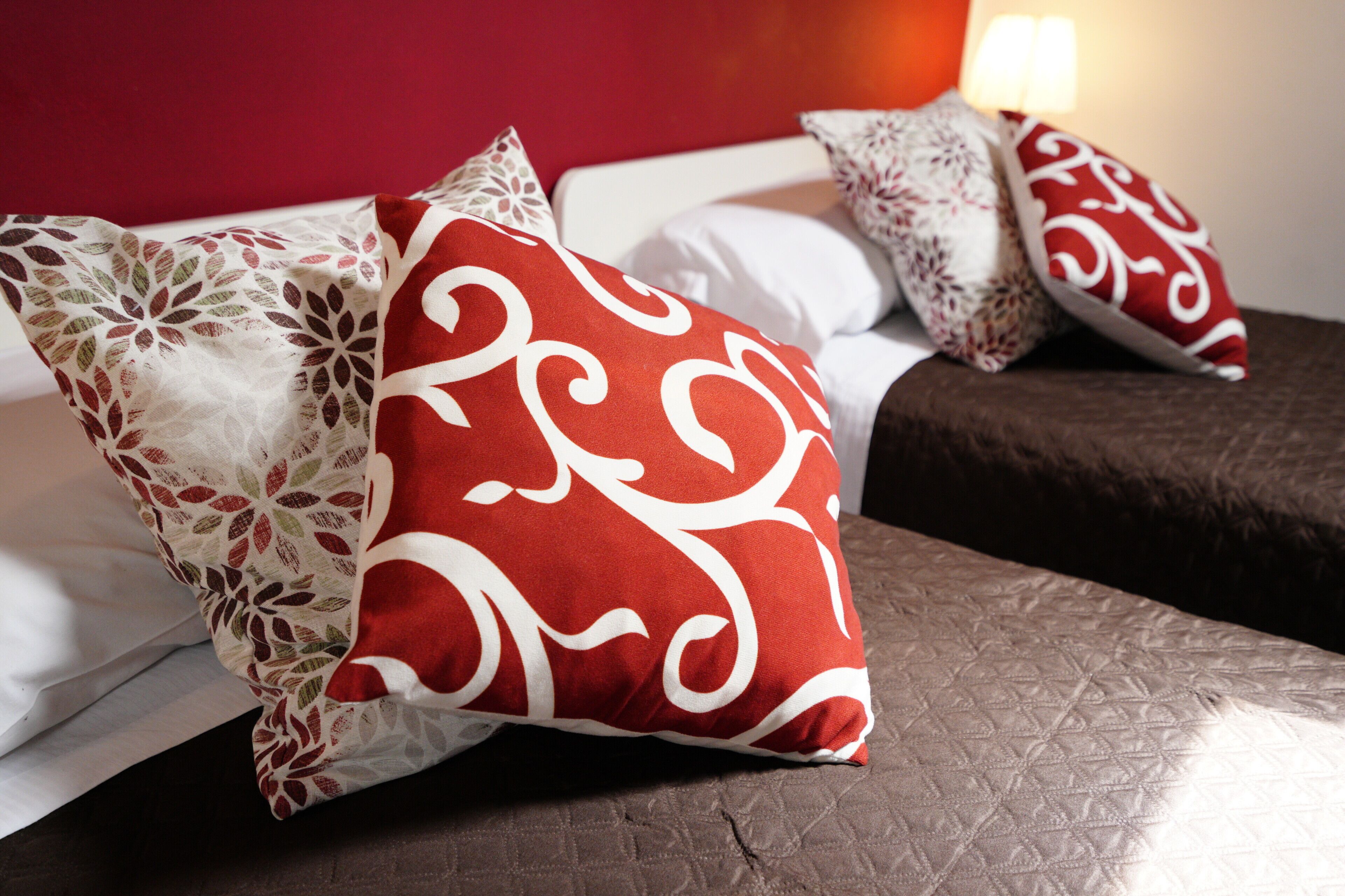 Un lit avec plusieurs oreillers, un matelas matelassé et un mur rouge.