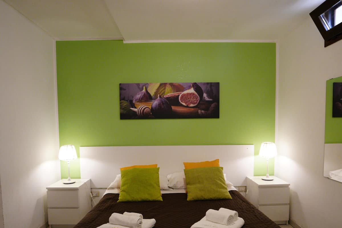 A bedroom with a bed, two nightstands, a green wall, and a ceiling light.