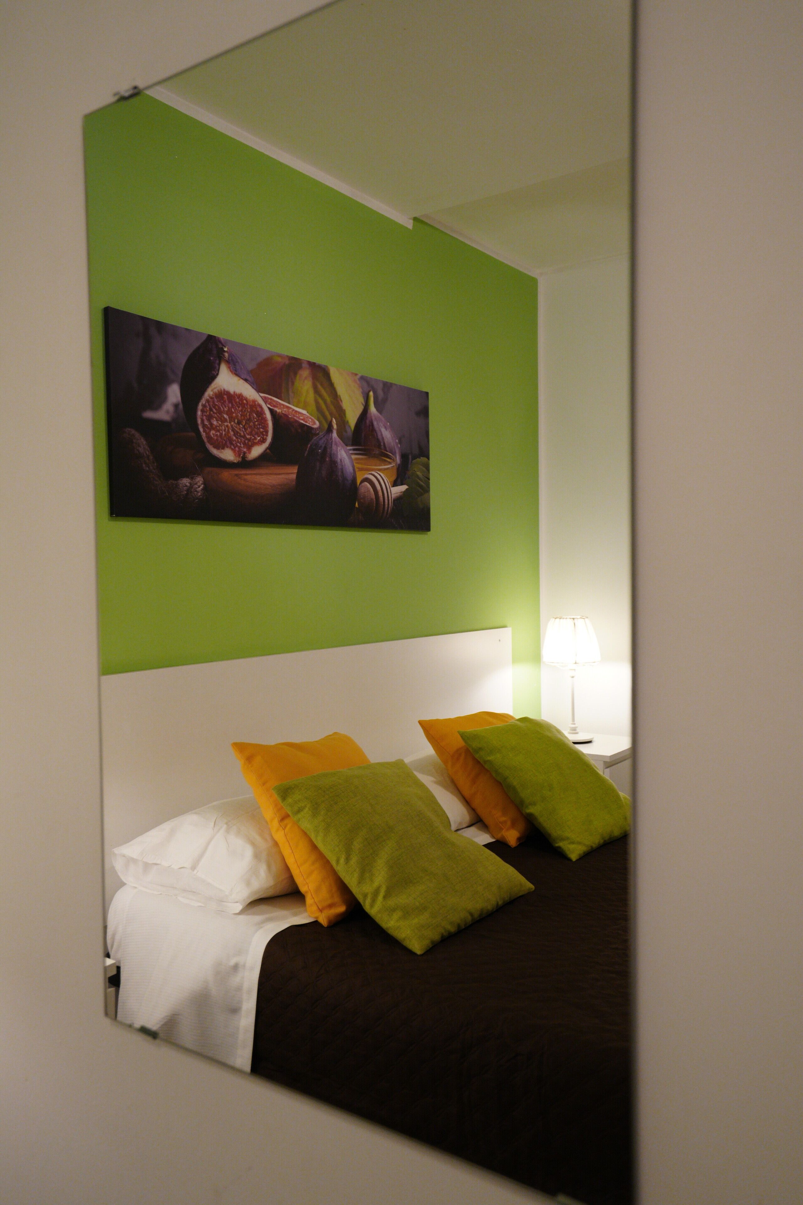 A hotel room with a bed, green walls, a painting, and a nightstand with a lamp.