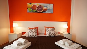 Habitación de hotel con colcha marrón, dos mesitas de noche blancas con lámparas, cabecero blanco y dos almohadas con estampado geométrico.