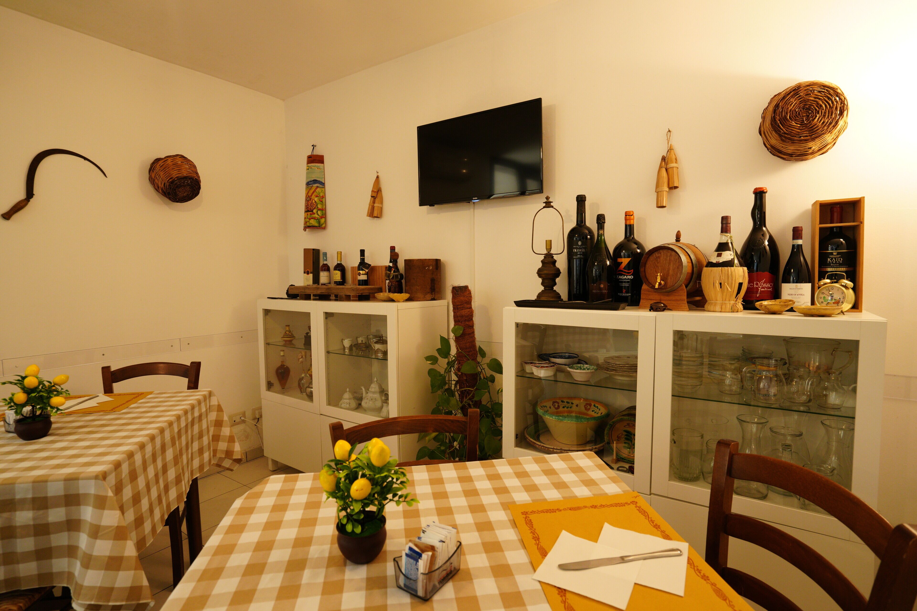 A dining area with checkered tablecloths, a potted lemon plant, and wine bottles on shelves.