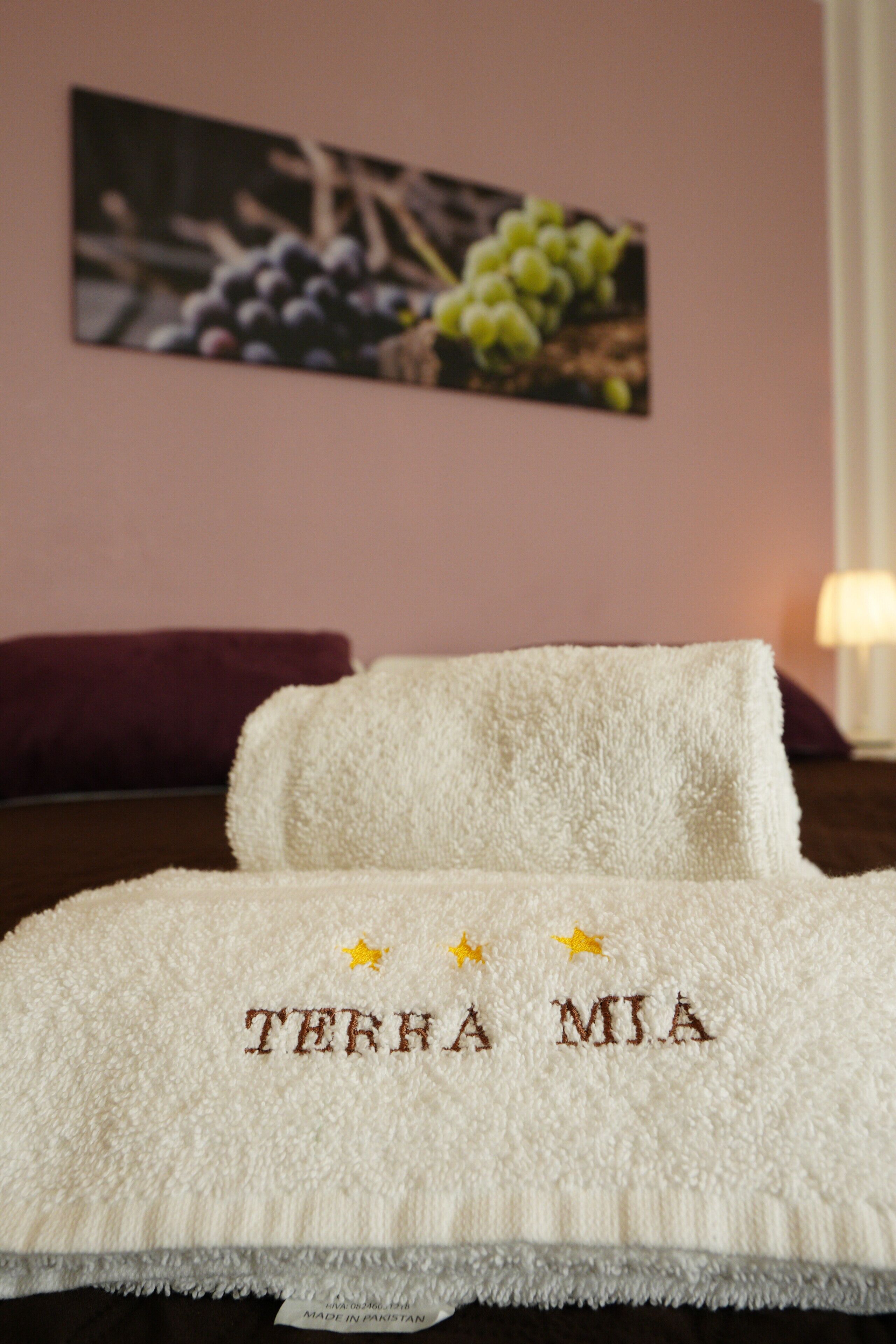 A neatly made bed with a white towel featuring embroidered text and a label stating 'MADE IN PAKISTAN'.