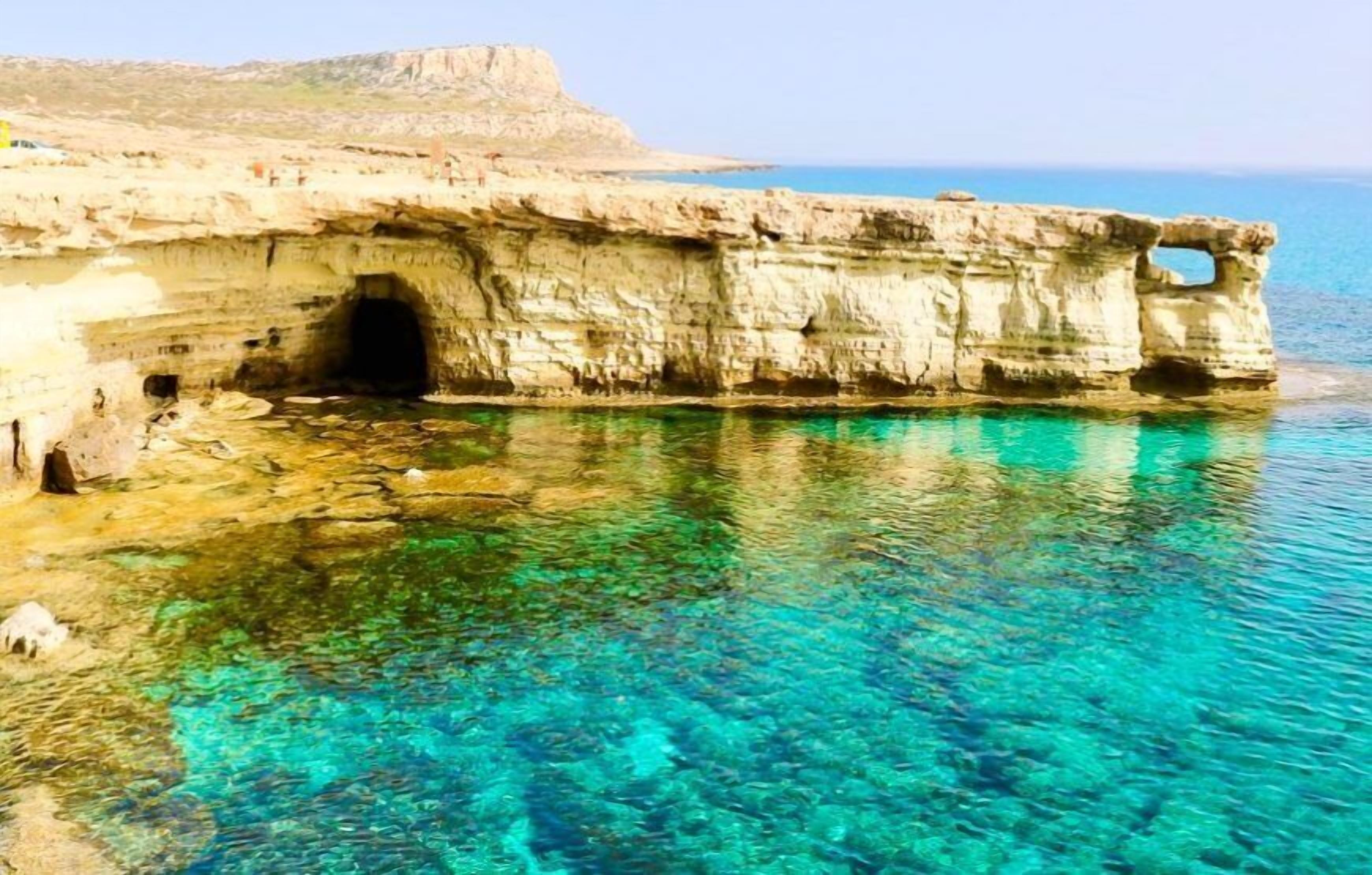 Ingang van een kustgrot met helder turquoise water en een rotsachtige klif.