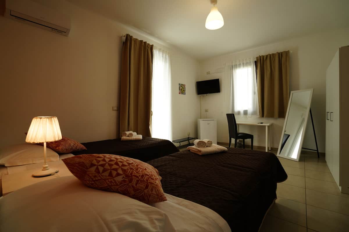 A hotel room with two beds, a desk, a chair, a TV, and an air conditioning unit.