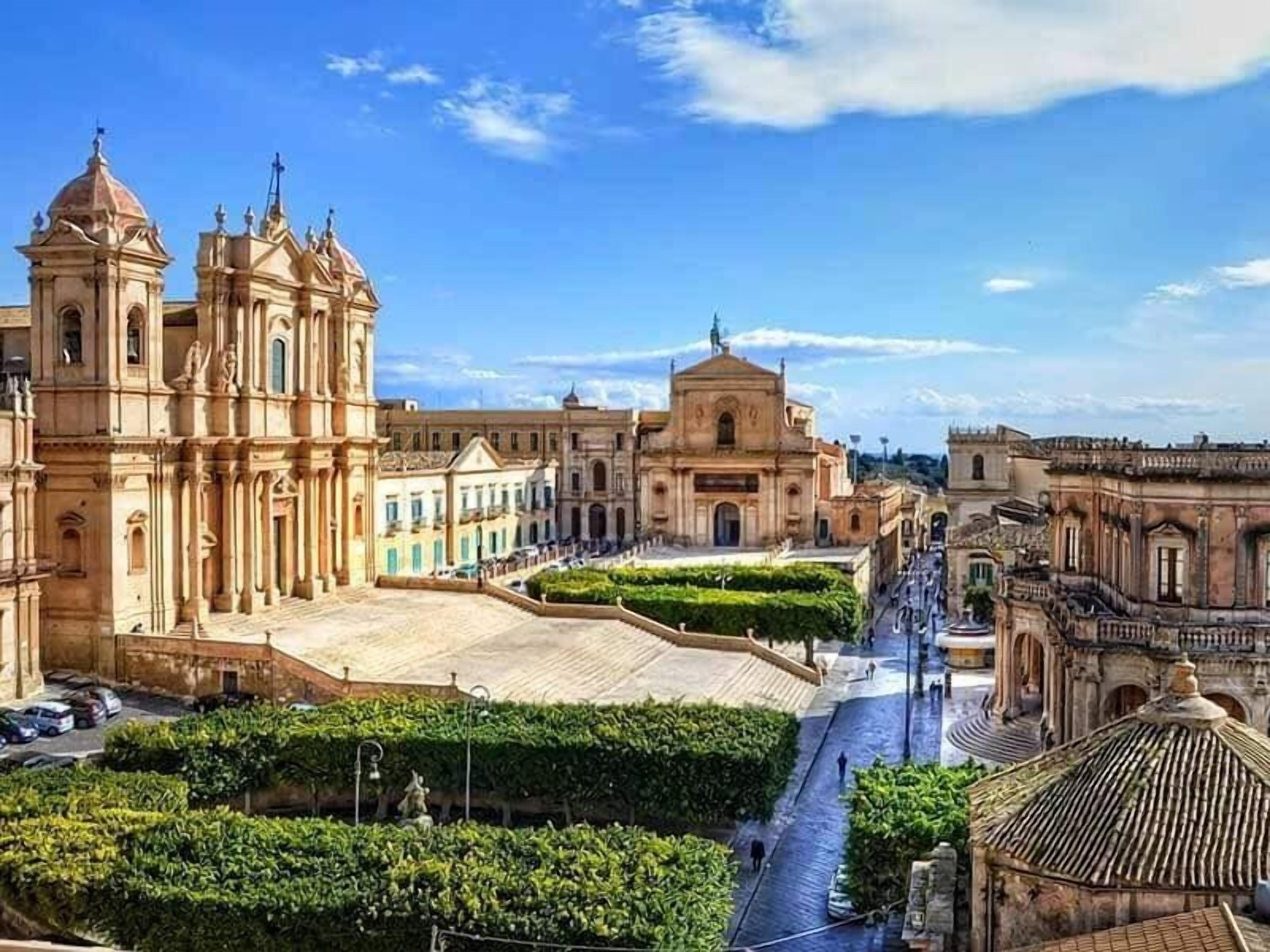 A historic plaza with classical architecture, including a prominent church with a dome and columns, a central square, and surrounding buildings.