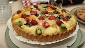Una torta di frutta su un piatto, con un tovagliolo a scacchi sotto, circondata da altri cibi.