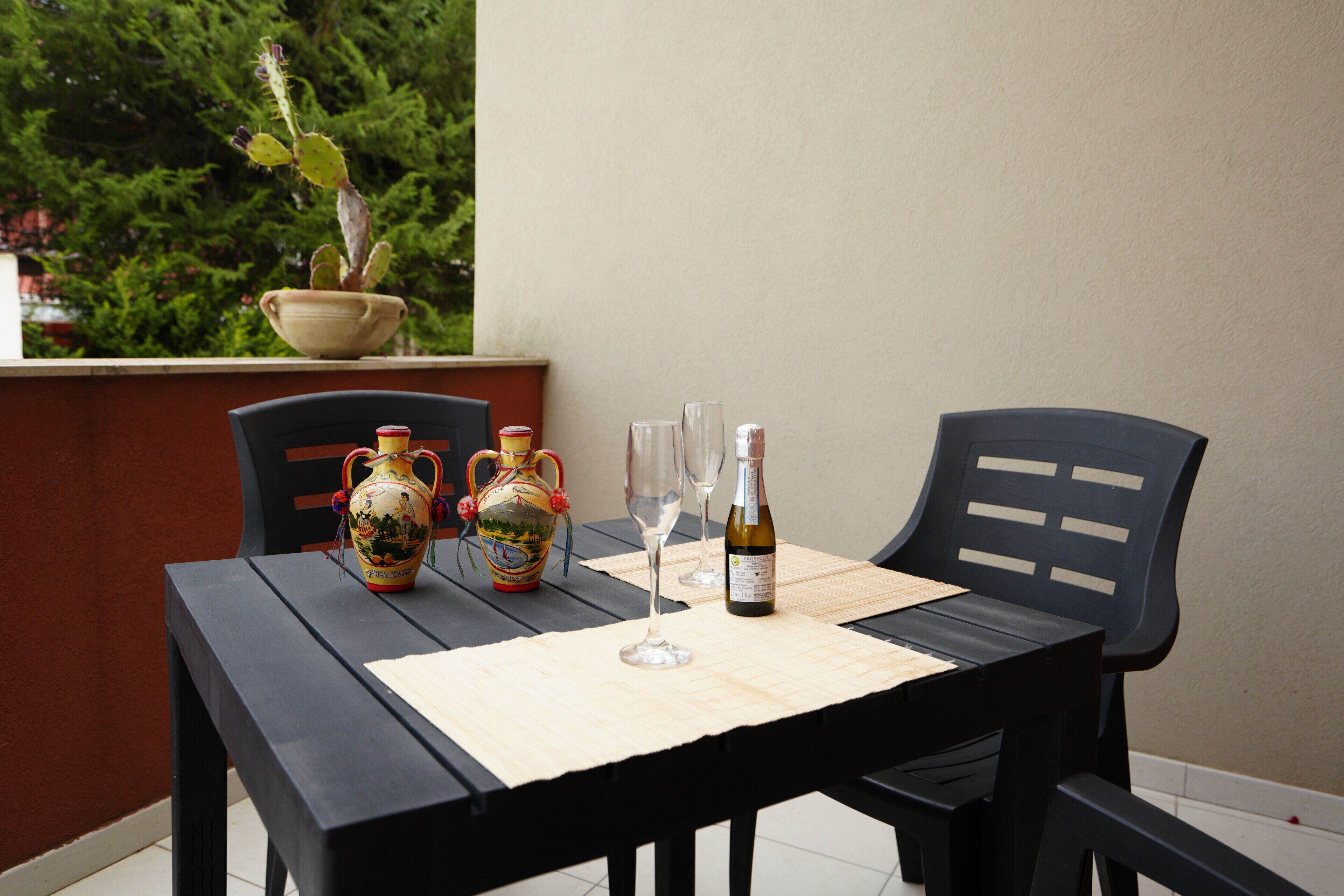 A table with a vase, two wine glasses, and a bottle on a tablecloth.