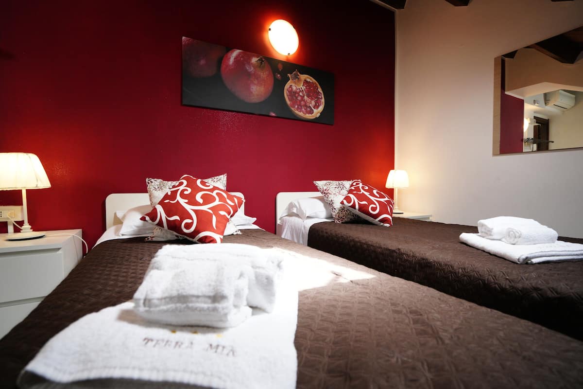 A hotel room with two beds, red walls, a fruit-themed wall decoration, and a mirror.