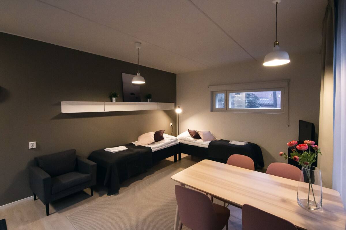 A modern hotel room with two single beds, a sofa, a dining table, and a small seating area.