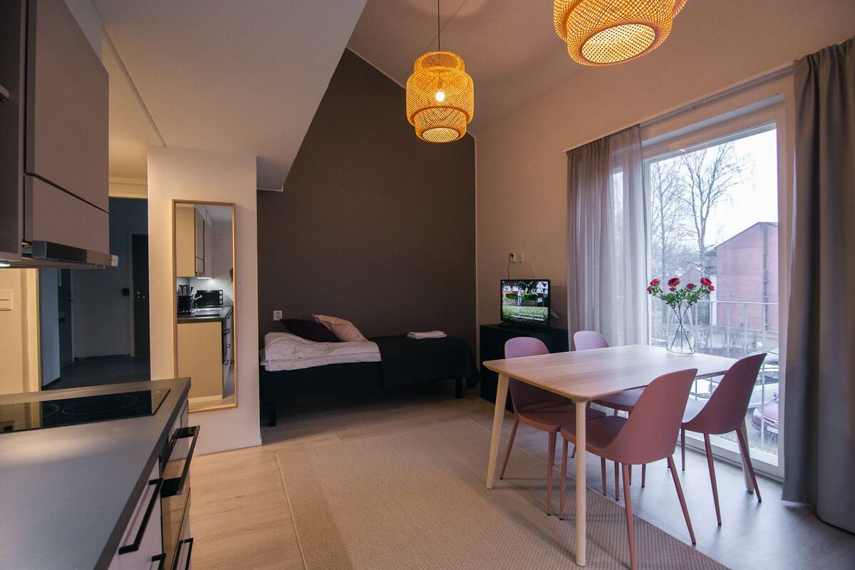 A modern hotel room with a kitchenette, a dining area, a bed, and a TV.