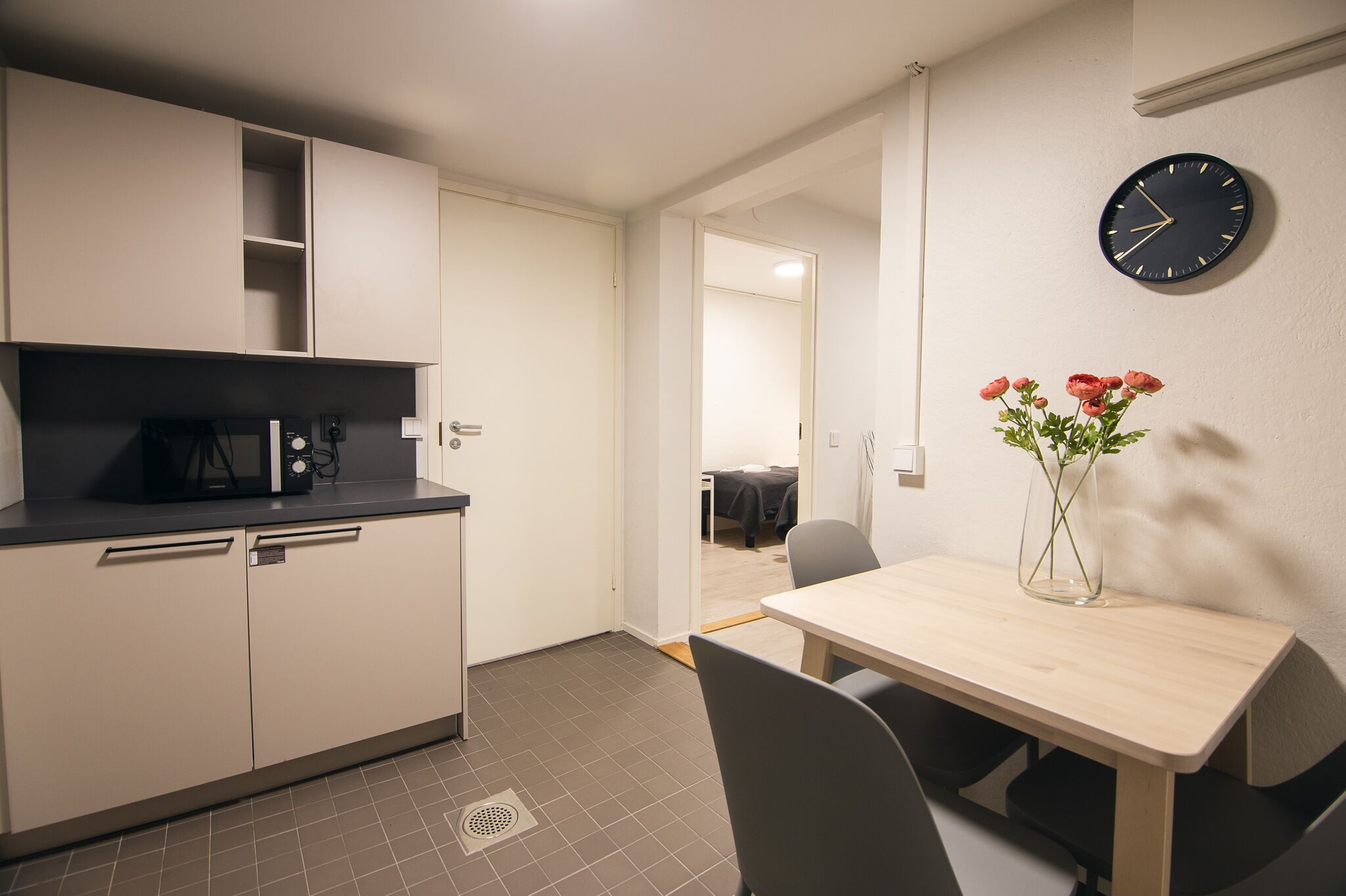 Una cocina compacta con microondas, una mesa de comedor con sillas y un florero con flores en la pared.